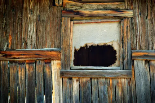 an old ripped hessian curtain in a log cabin window