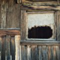 window of a log cabin with ripped hessian curtain